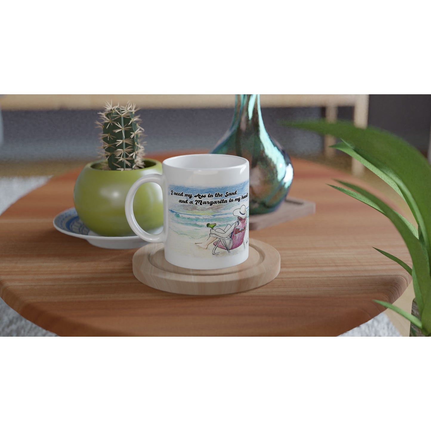 A white ceramic 11oz mug with motto I need my Ass in the Sand and a Margarita in my hand on front and WhatYa Say logo on back dishwasher and microwave safe from WhatYa Say Apparel sitting on coaster with green potted cactus and silver vase. 