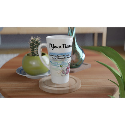 A personalized Seventeener white ceramic 17oz mug with personalized original motto [Enter Name] I need my Ass in the Sand and a Margarita in my hand on front and WhatYa Say logo on back dishwasher and microwave safe from WhatYa Say Apparel sitting on coaster on coffee table with green potted cactus and silver vase.
