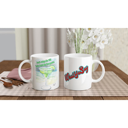 Two white ceramic 11oz mugs with motto Don't Judge Me till You've Held my Margarita on front and WhatYa Say logo on back coffee mugs are dishwasher and microwave safe from WhatYa Say Apparel sitting on coffee table with placemat.