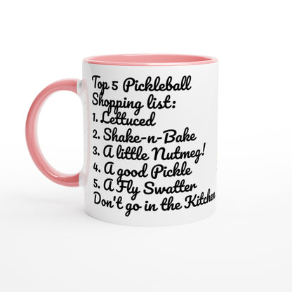White ceramic 11oz mug with pink handle original motto Top 5 Pickleball Shopping list lettuce, Shake-n-bake, Nutmeg, Pickle, a Fly Swatter Don’t go in the kitchen front side and Let's Play PickleBall logo on back dishwasher and microwave safe ceramic coffee mug from WhatYa Say Apparel front view.