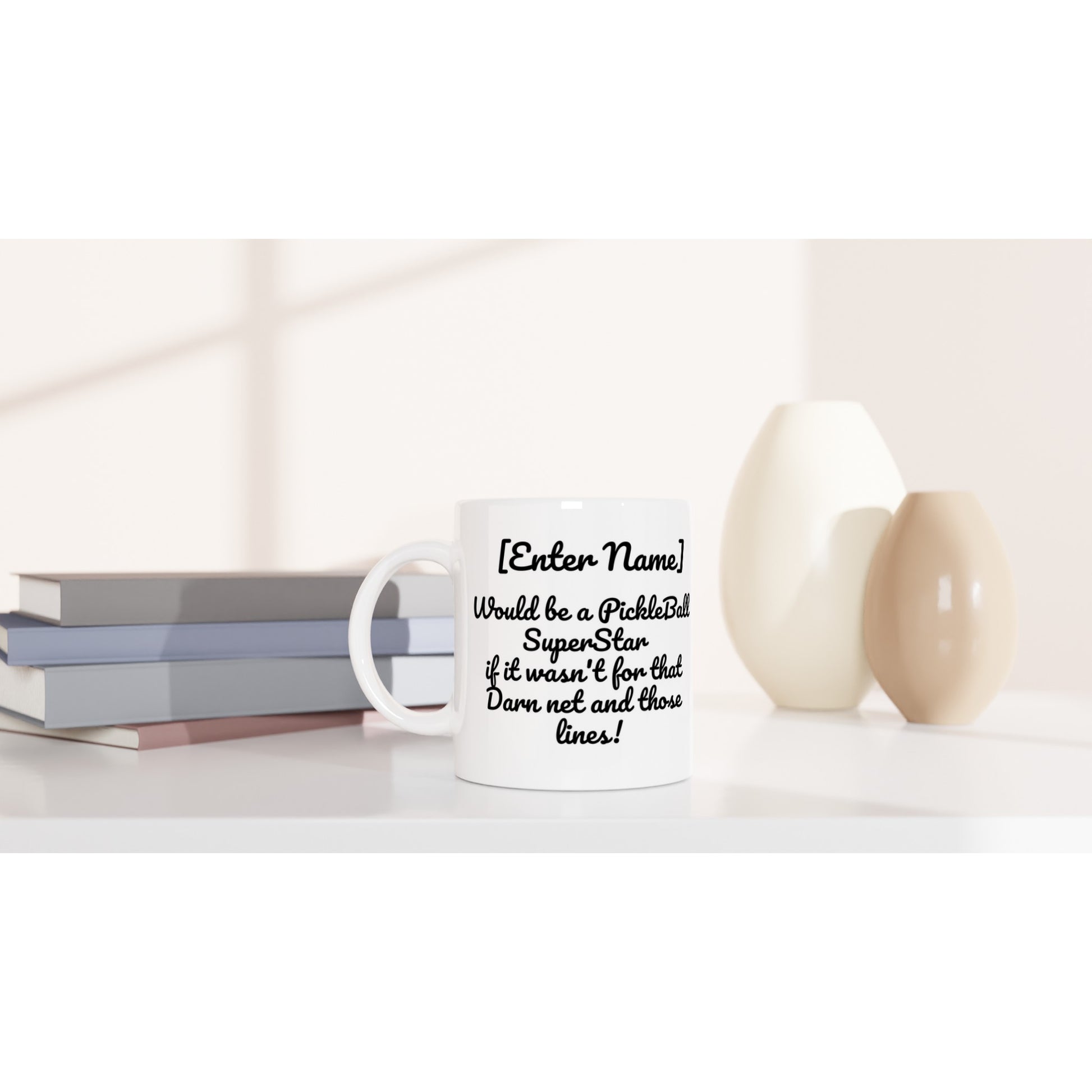 Personalized white ceramic 11oz mug with personalized motto Your Name Would be a PickleBall Superstar if it wasn’t for that Darn net and those lines on front and Let's Play Pickleball logo on back dishwasher and microwave safe from WhatYa Say Apparel sitting on coffee table with books and two vases. 