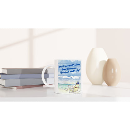 A white ceramic 11oz mug with motto funny saying Don't borrow Problems from Tomorrow... You don't need Today! on front and WhatYa Say logo on back dishwasher and microwave safe from WhatYa Say Apparel sitting on coffee table with books and two vases.