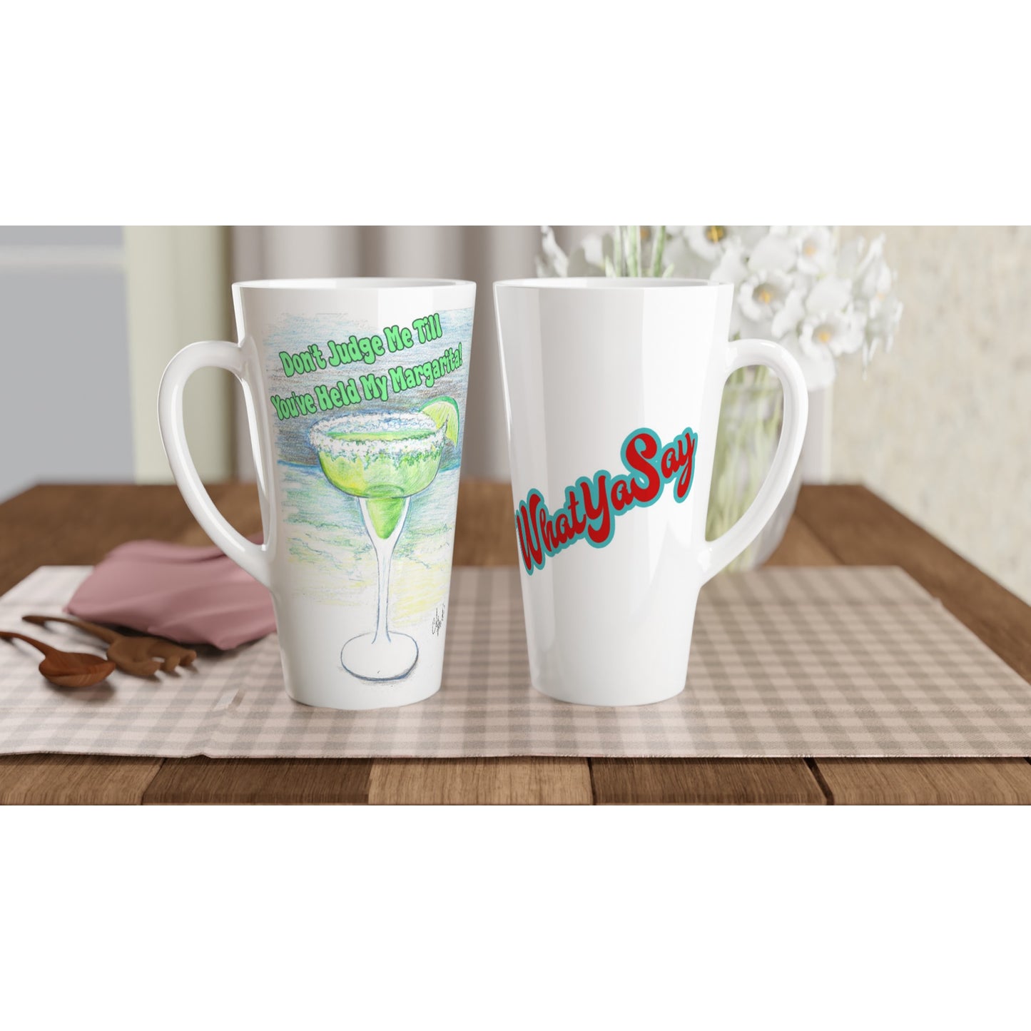 Two Seventeener white ceramic 17oz mugs with motto Don't Judge Me till You've Held my Margarita on front and WhatYa Say logo on back dishwasher and microwave safe from WhatYa Say Apparel sitting on coffee table with green and white placemat.