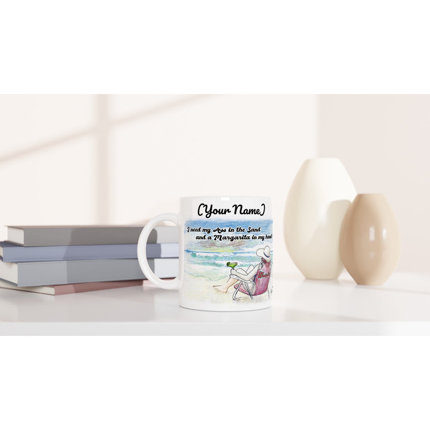 Personalized white ceramic 11oz mug with original personalized motto [Your Name] I need my Ass in the Sand and a Margarita in my hand on the front and WhatYa Say logo on the back dishwasher and microwave safe from WhatYa Say Apparel sitting on coffee table with books and two vases.