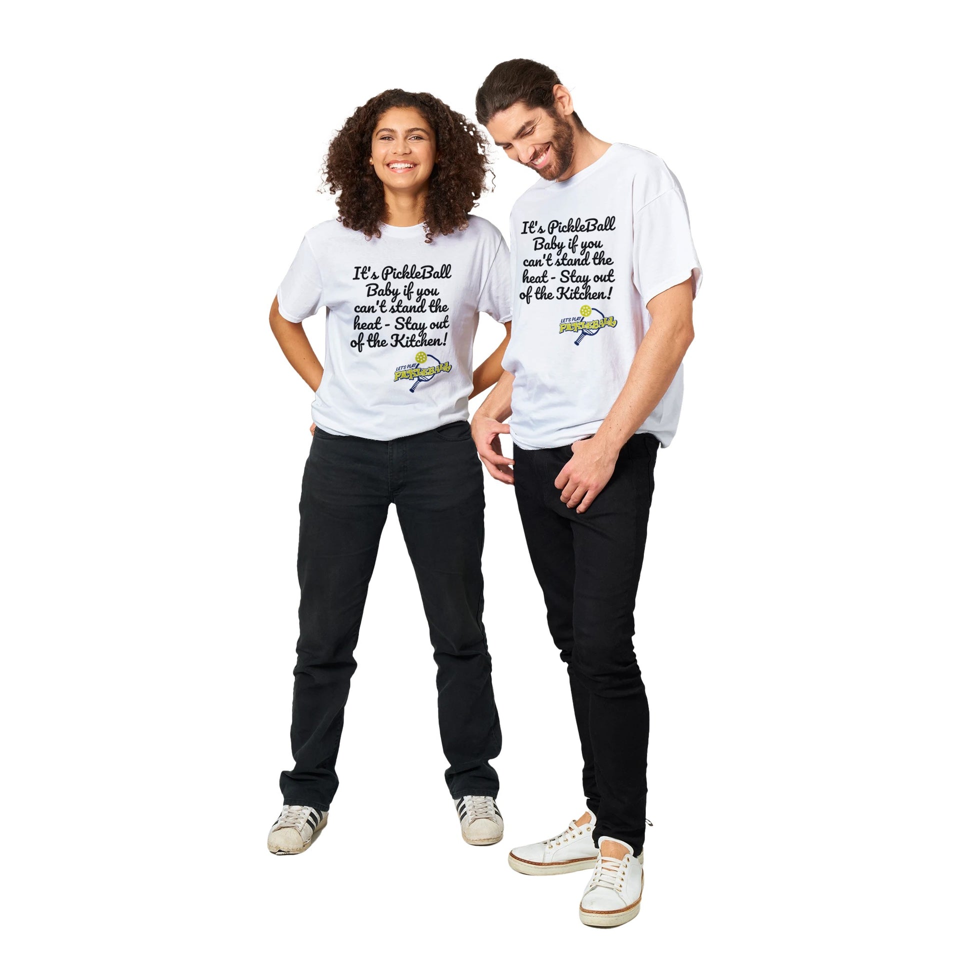 A white comfortable Unisex Crewneck heavyweight cotton t-shirt with funny saying It’s PickleBall Baby if can’t stand the heat – Stay out of the Kitchen!  and Let’s Play Pickleball logo on the front from WhatYa Say Apparel worn by Happy woman and man couple standing side by side.