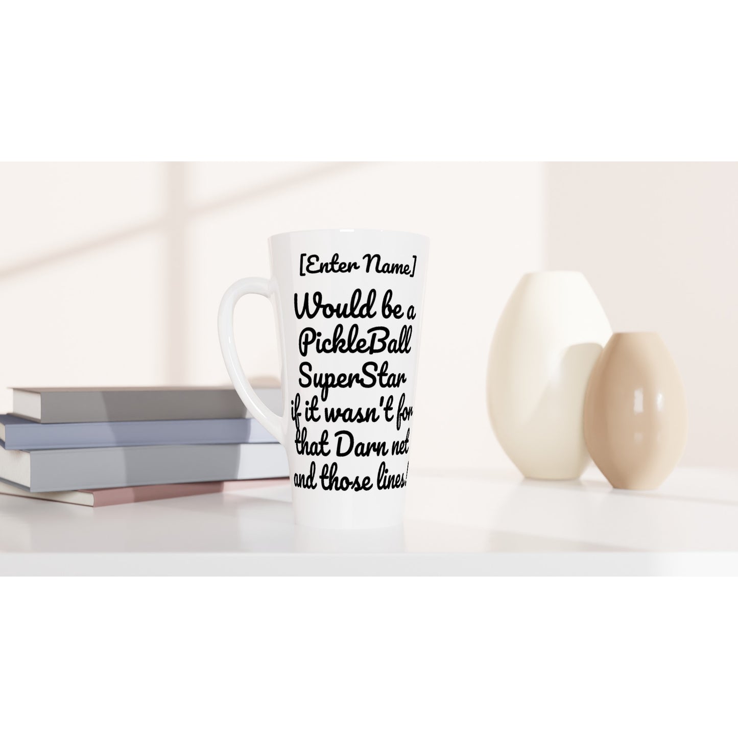Personalized Seventeener white ceramic 17oz mug with original personalized motto [Your Name] ] Would be a PickleBall SuperStar if it wasn’t for that Darn net and those lines! on front and Let’s Play Pickleball logo on back coffee mug dishwasher and microwave safe from WhatYa Say Apparel sitting on coffee table with books and two vases.
