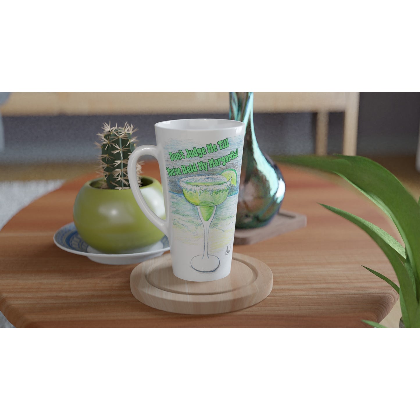 A Seventeener white ceramic 17oz mug with motto Don't Judge Me till You've Held my Margarita dishwasher and microwave safe from WhatYa Say Apparel sitting on coaster on coffee table with green potted cactus and silver vase.