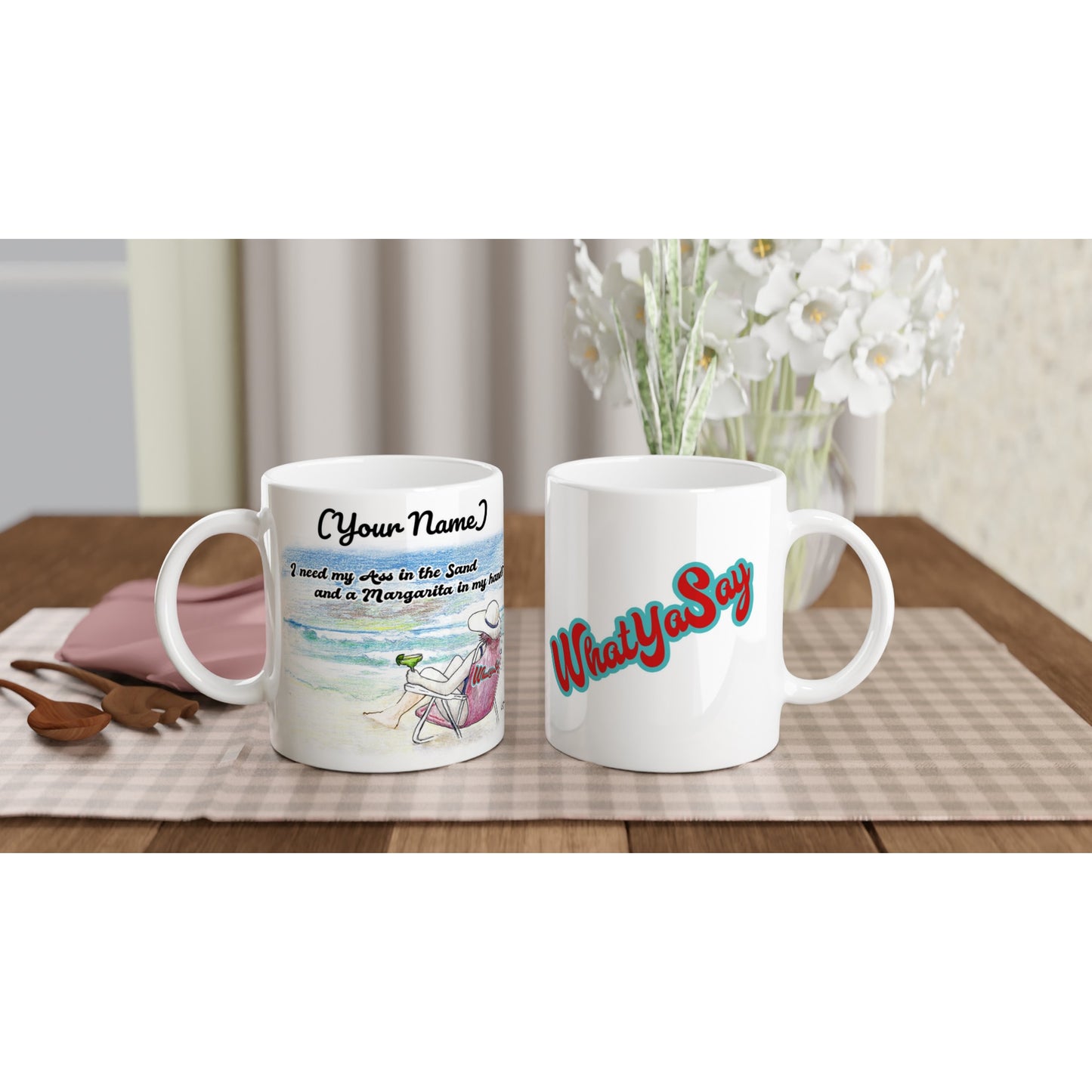 Two Personalized white ceramic 11oz mugs with original personalized motto [Your Name] I need my Ass in the Sand and a Margarita in my hand on the front and WhatYa Say logo on the back coffee mugs are dishwasher and microwave safe from WhatYa Say Apparel sitting on coffee table with green and white placemat.