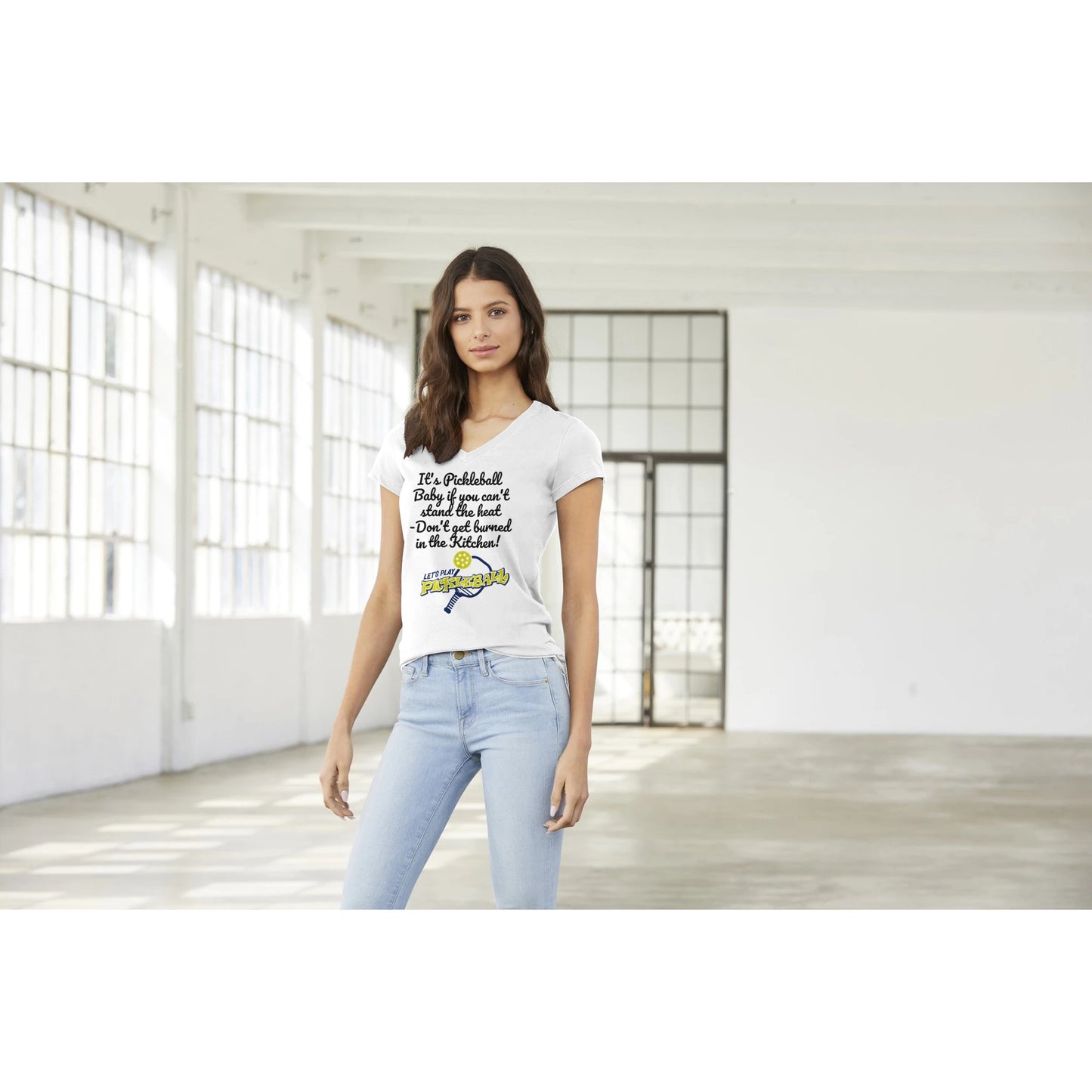 A premium women’s V-neck t-shirt from combed and ring-spun cotton original logo It's PIckleball Baby if you can't stand the heat - Don't get burned in the Kitchen and Let's Play PickleBall on front worn by a dark-haired female model standing.